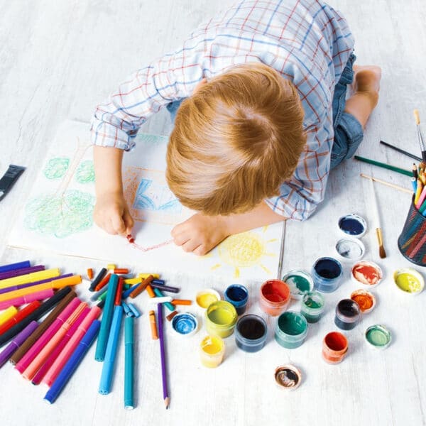 Egy gyerek zsírkrétákkal játszik a padlón.